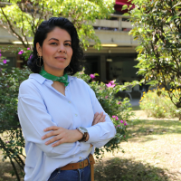 Foto de la profesora Edel Sánchez. Al fondo tiene árboles. Tiene una camisa azul clara y una pañoleta verde en el cuello.