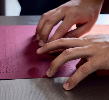 manos tocando hoja con texto Braille.