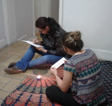 dos mujeres sentadas en el suelo, leyendo con vela encendida.