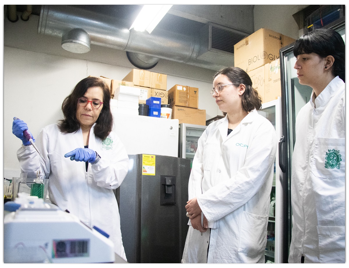 Tres mujeres en un laboratorio, con batas blancas, llevando a cabo un experimento. una de ellas tiene guantes azules de latex, está manipulando un equipo para transferir líquido a un contenedor