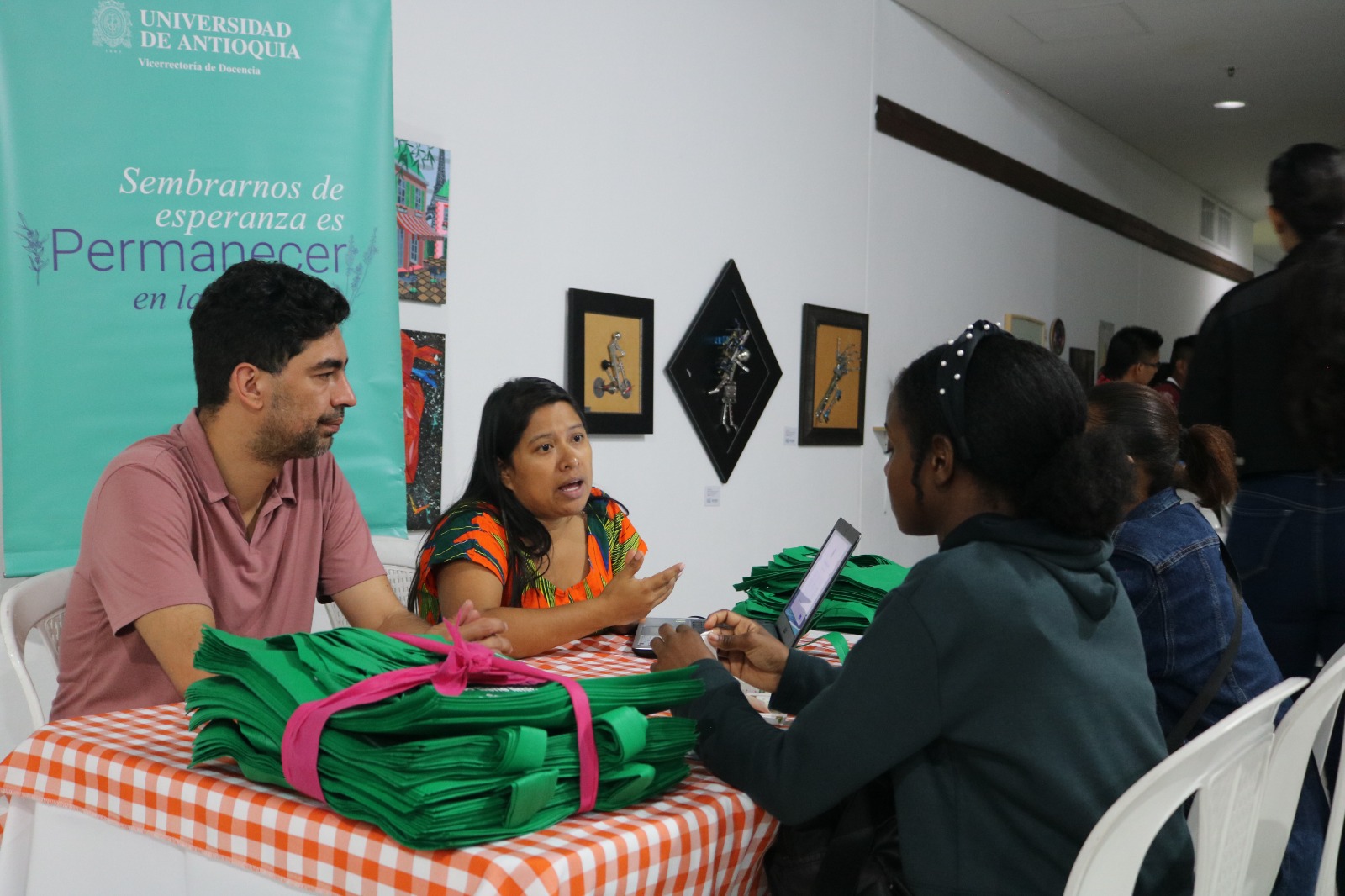 Foto: Un grupo de cuatro personas están sentadas en el stand de la Universidad de Antioquia, cada una en una silla, alrededor de una mesa con mantel de cuadros.