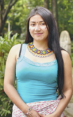 Profesora indígena êbêra Chamí de largo cabello, con vestido tradicional de flores, collar de colores en mostacilla y con su rostro pintado con símbolos tradicionales en jagua.